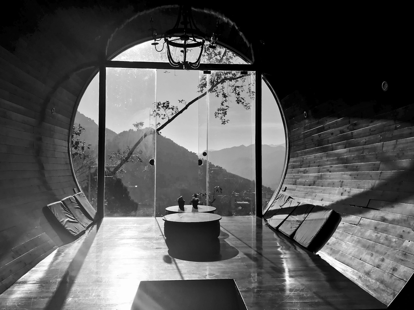 Curved wooden room with cushions overlooking a mountain landscape.