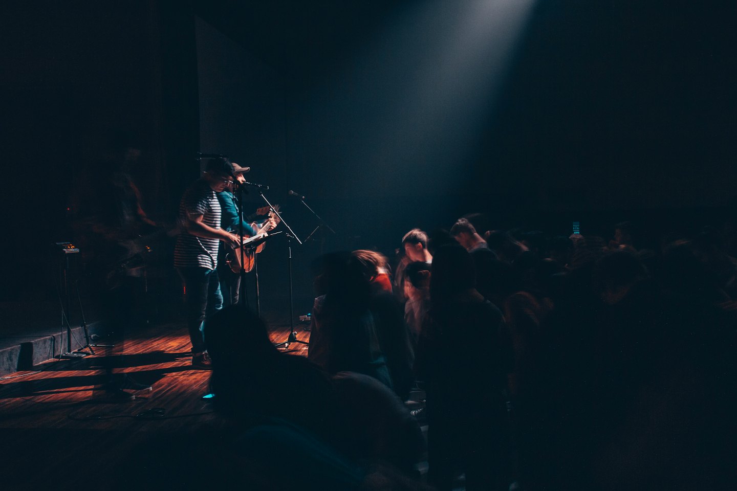Two musicians play guitar on a brightly lit stage.